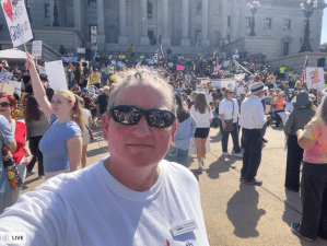 Kasie with sunglasses in front of the state house with a crowd